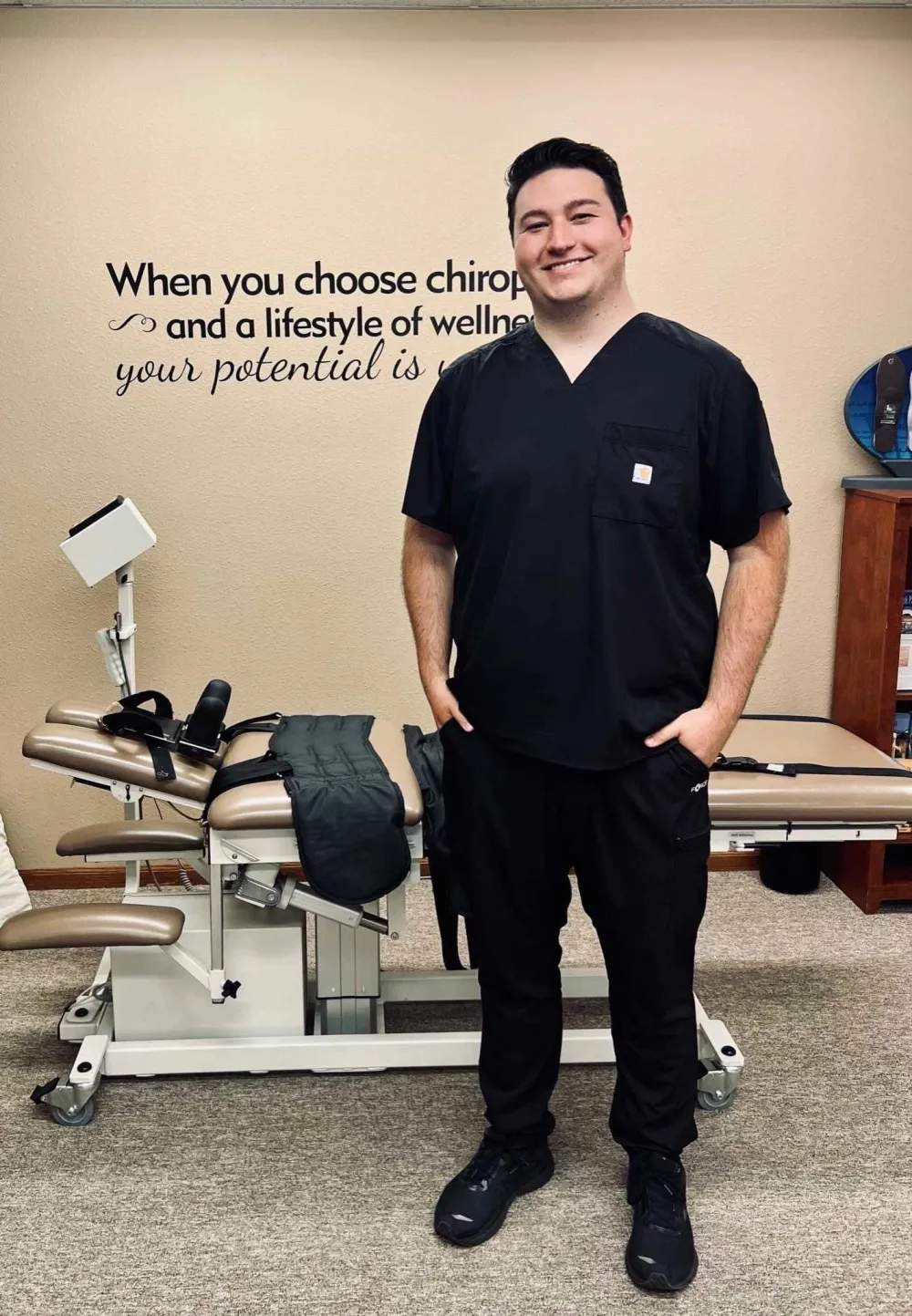 Dr. Austin Stutzman in black scrubs, standing in the clinic in front of a treatment table