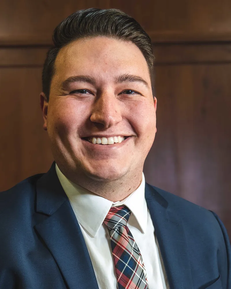Dr. Austin Stutzman smiling, in a navy suit and plaid tie